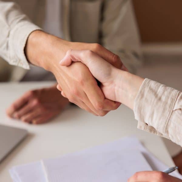 Two unrecognizable individuals are shaking hands in a professional office setting, symbolizing a successful business agreement, cooperation, or the start of a new partnership