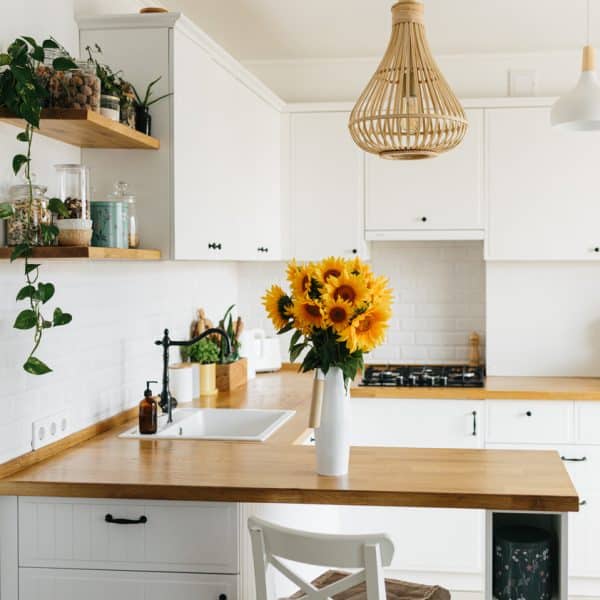 View on clean white simple modern kitchen in scandinavian style, kitchen details, wooden table, sunflowers bouquet in vase on the table