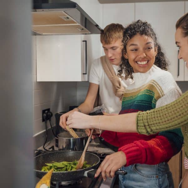 Students cooking together at their university housing in Newcastle, North East England. They are talking and smiling while they make dinner in their shared open plan kitchen.