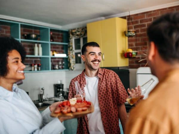 A group of friends relaxing and enjoying a selection of snacks and drinks served on a wooden board during a casual home gathering. cheerful moments and a friendly vibe in a cozy setting