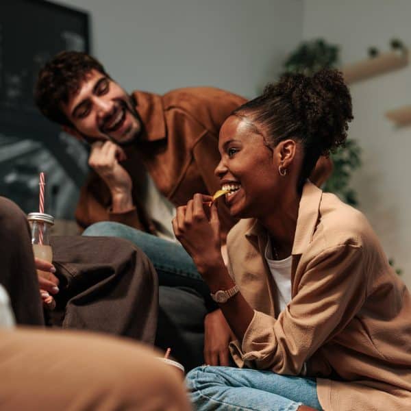 A warm, relaxed living room scene with diverse friends chatting and laughing while enjoying drinks and snacks. Cozy atmosphere highlights friendship, sociability, and casual everyday moments.